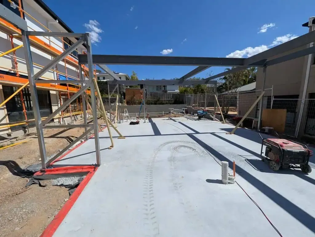 Construction site with steel framing, concrete slab, and red safety barriers under a blue sky
