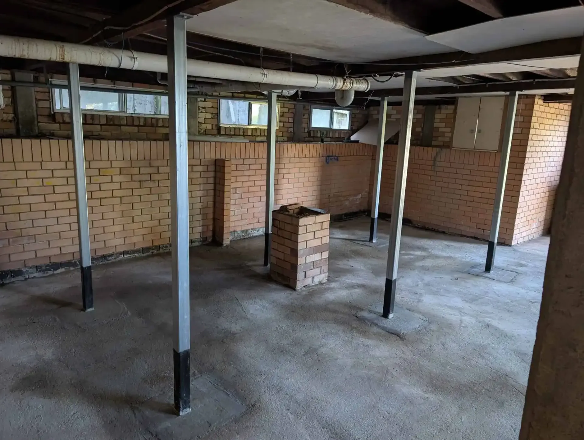 Unfinished basement with exposed brick walls, concrete floor, and support pillars.