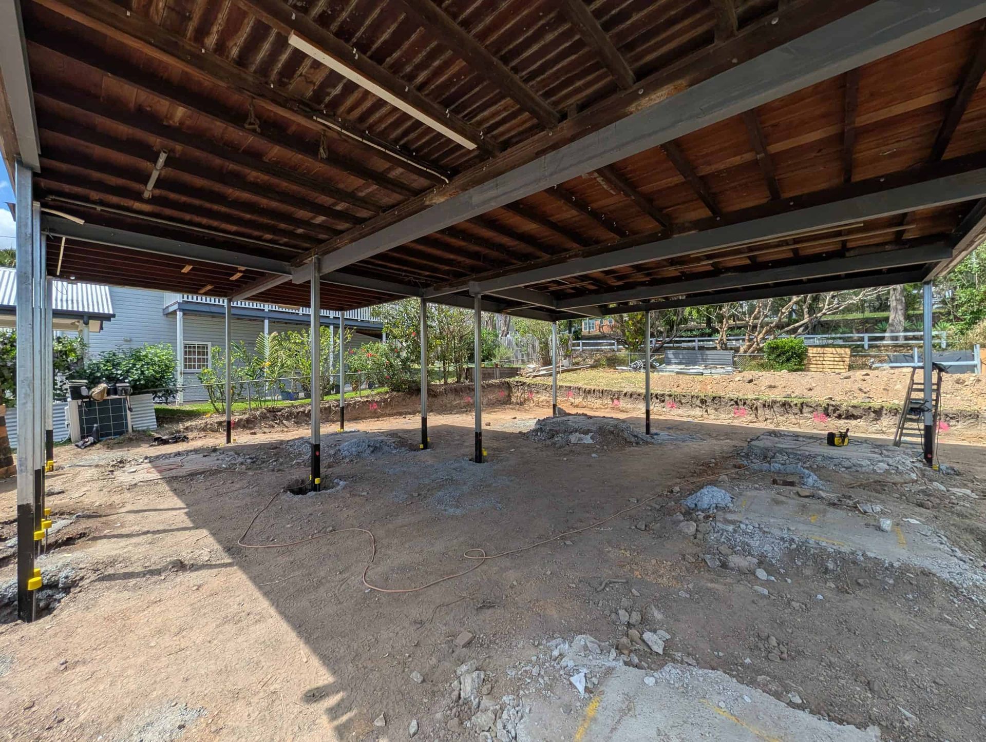Open-sided wooden shelter with a dirt floor and supporting posts in a rural setting.