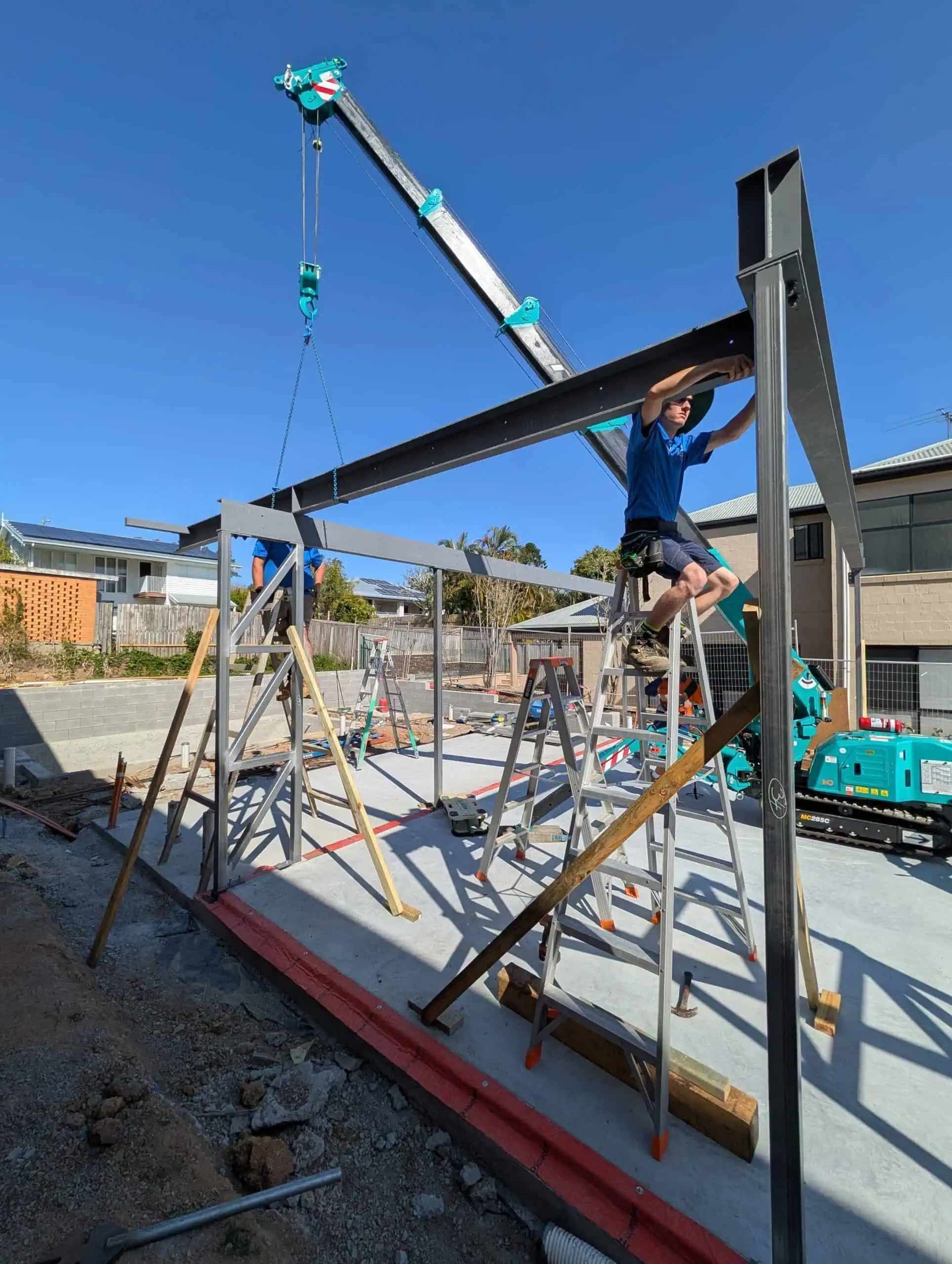 Worker on a construction site lifting a roof beam with a crane and scaffolding around the frame