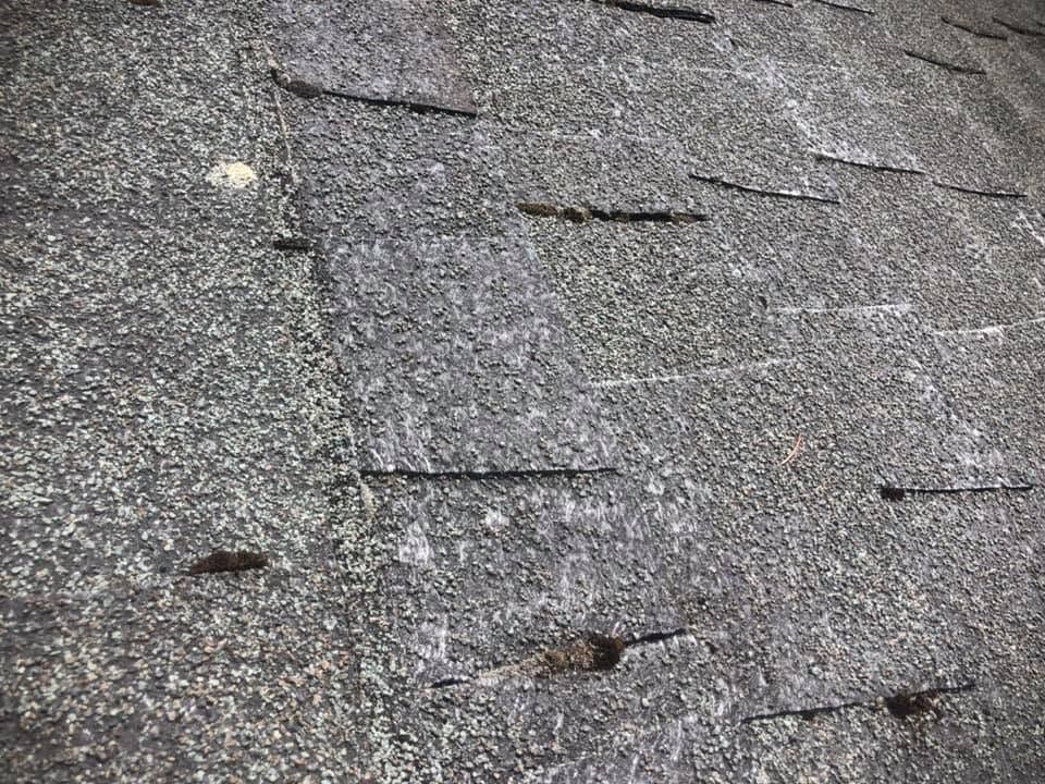 Damaged gray asphalt roof shingles with several missing and loose pieces