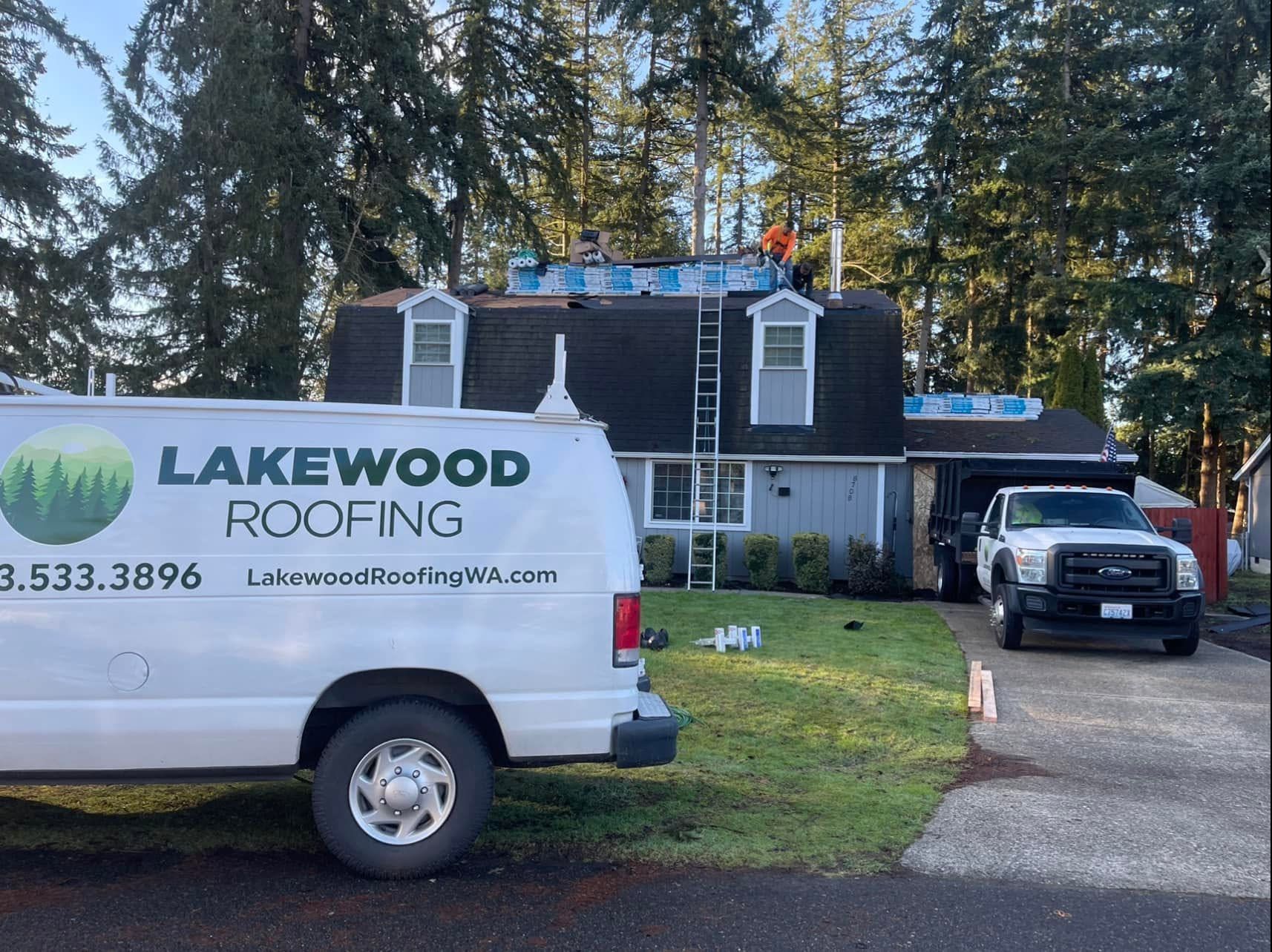 Lakewood Roofing van and pickup parked outside a house with roof work in progress, surrounded by trees.