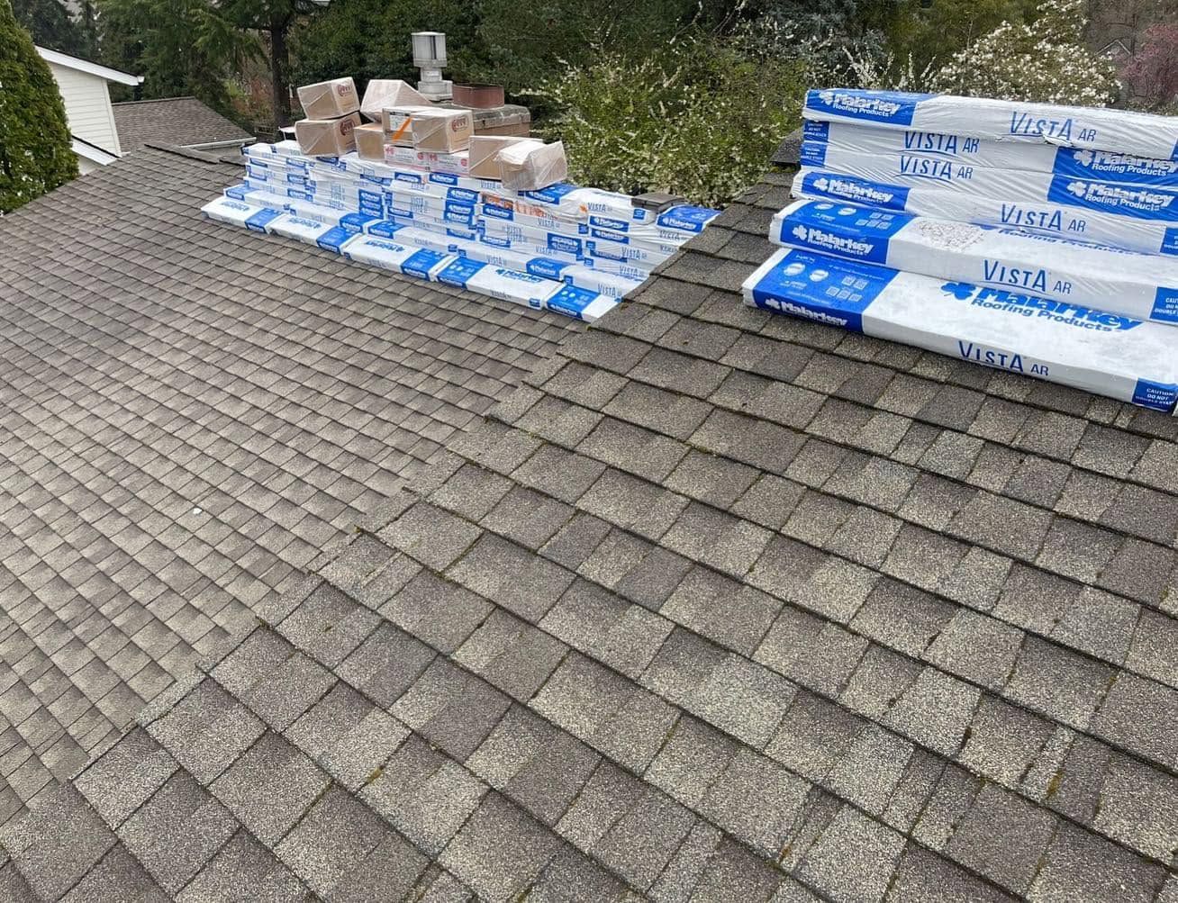 Roof shingles with stacked roofing materials near a chimney and a roof repair area