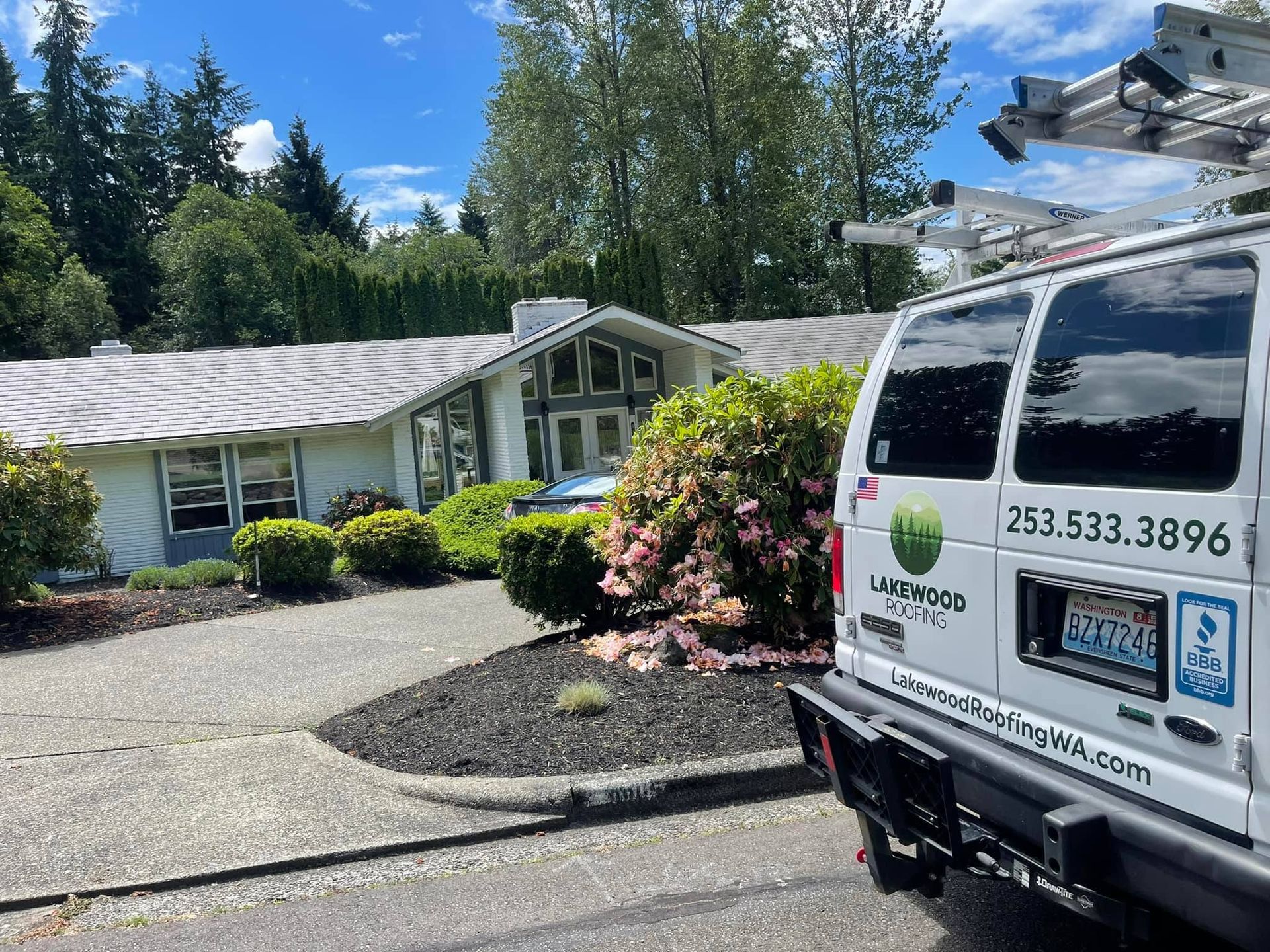 Landscaped house with a white service van parked in the driveway on a sunny day