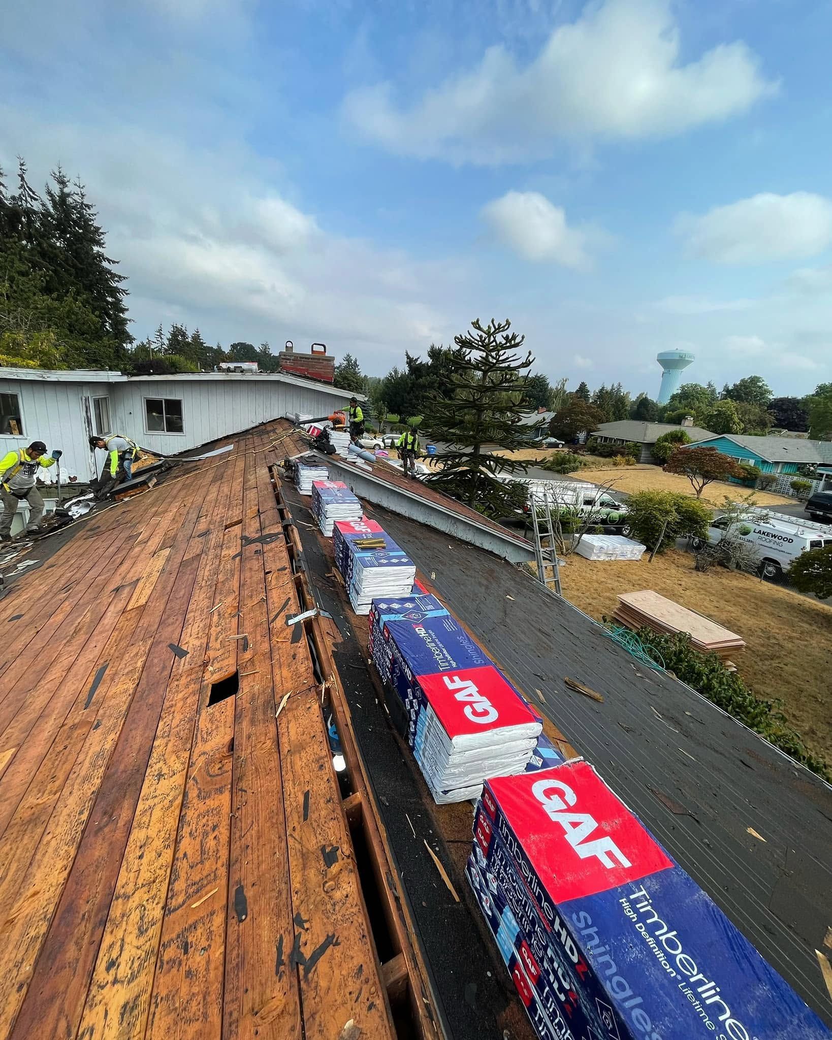 Rooftop repair with orange sheathing, red-and-blue tarps, and workers on a cloudy day