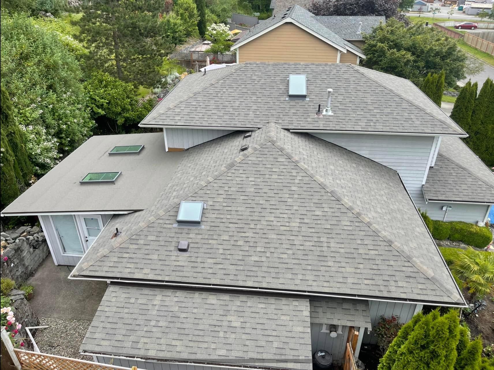 Aerial view of a gray-shingled house roof with skylights and surrounding trees