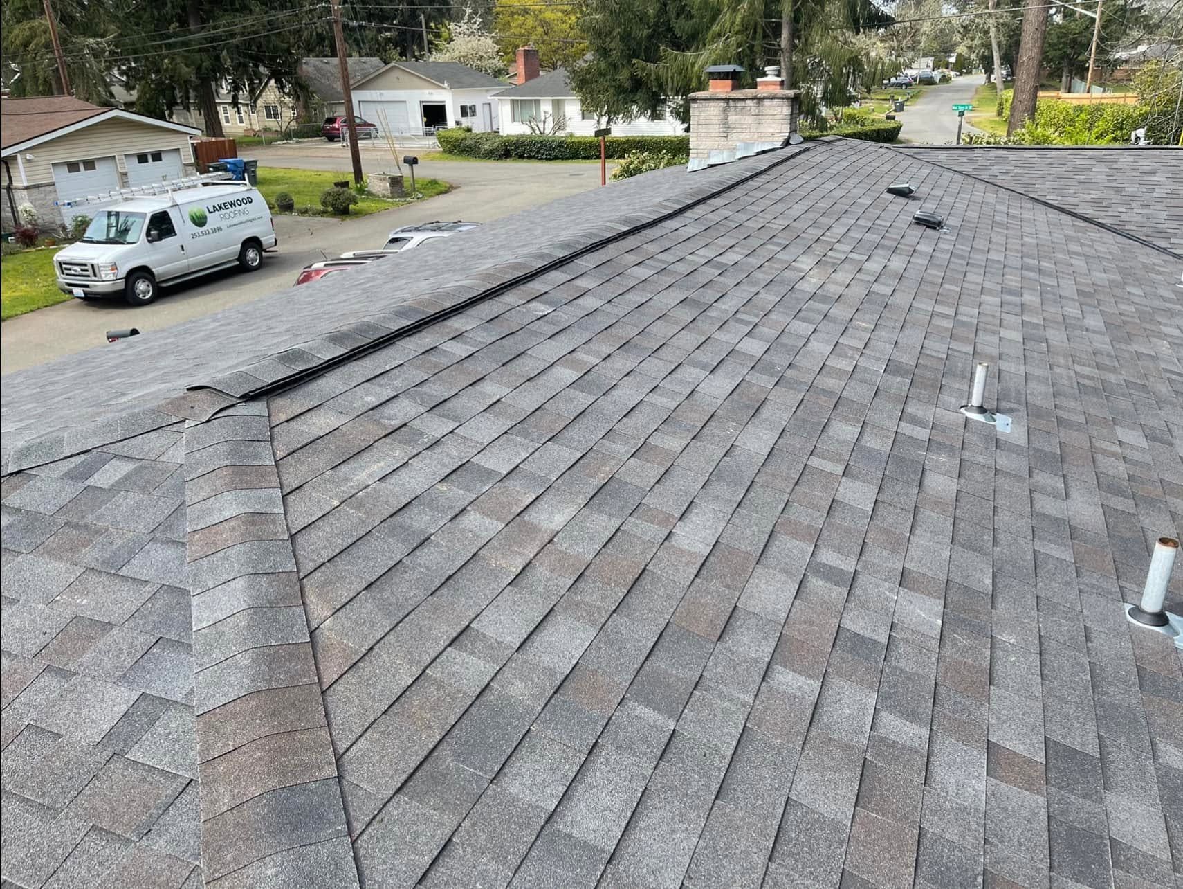 Gray shingle roof viewed from above, with a white utility truck and houses in the background.
