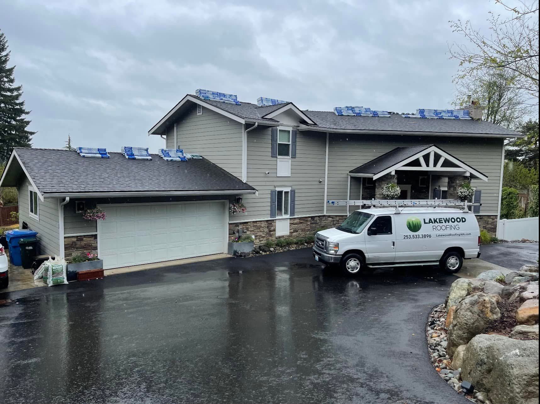 Rainy driveway with a white utility van parked beside a two-story house and detached garage