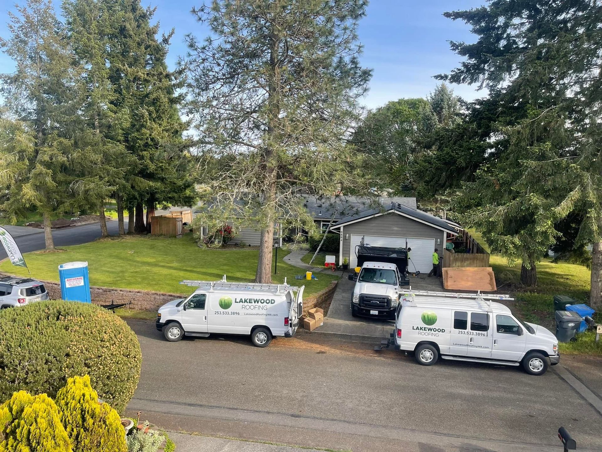 Two white work vans parked on a gravel driveway beside a garage and large trees
