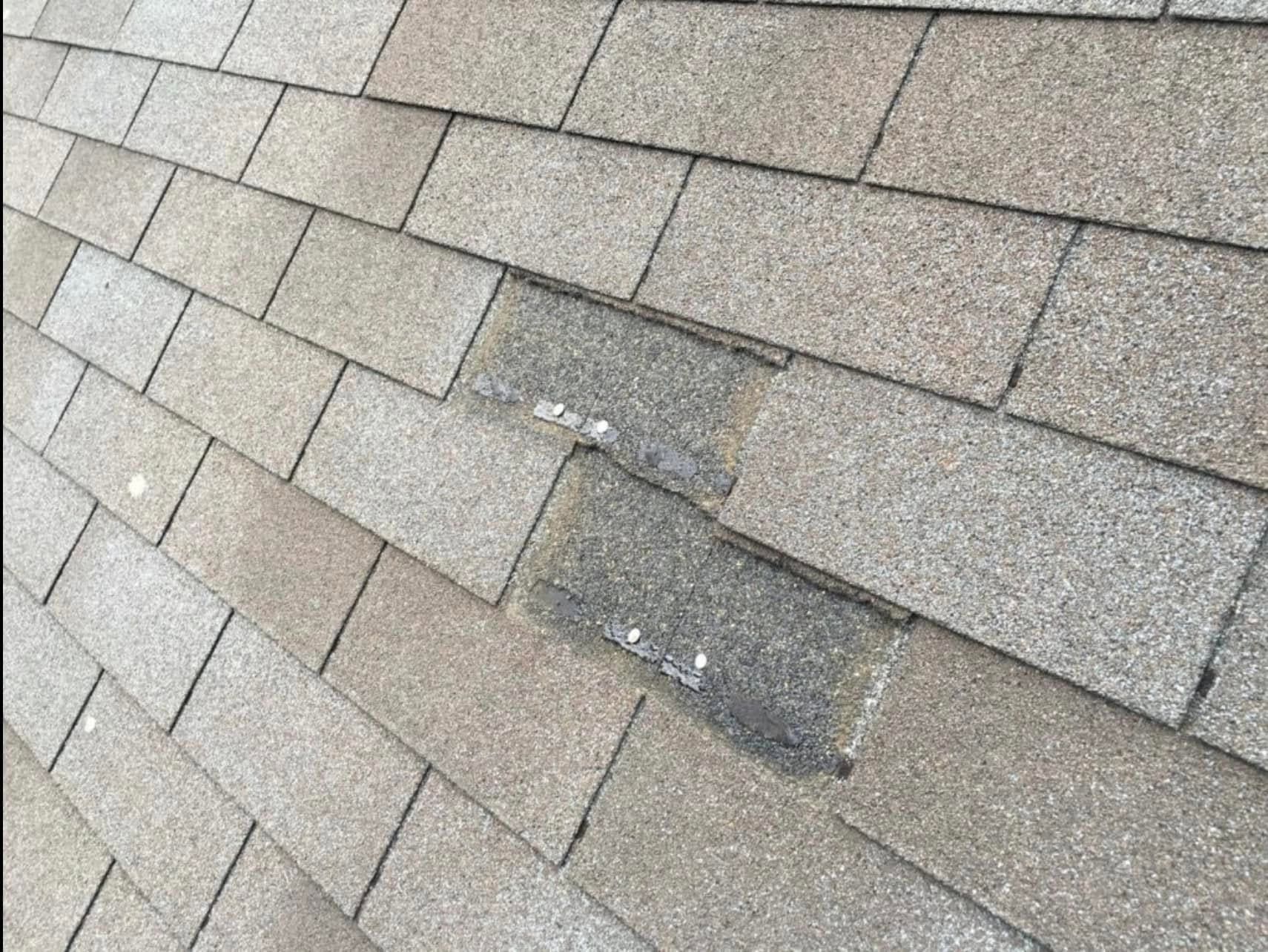 Damaged asphalt roof shingles with a dark patch and peeling granules
