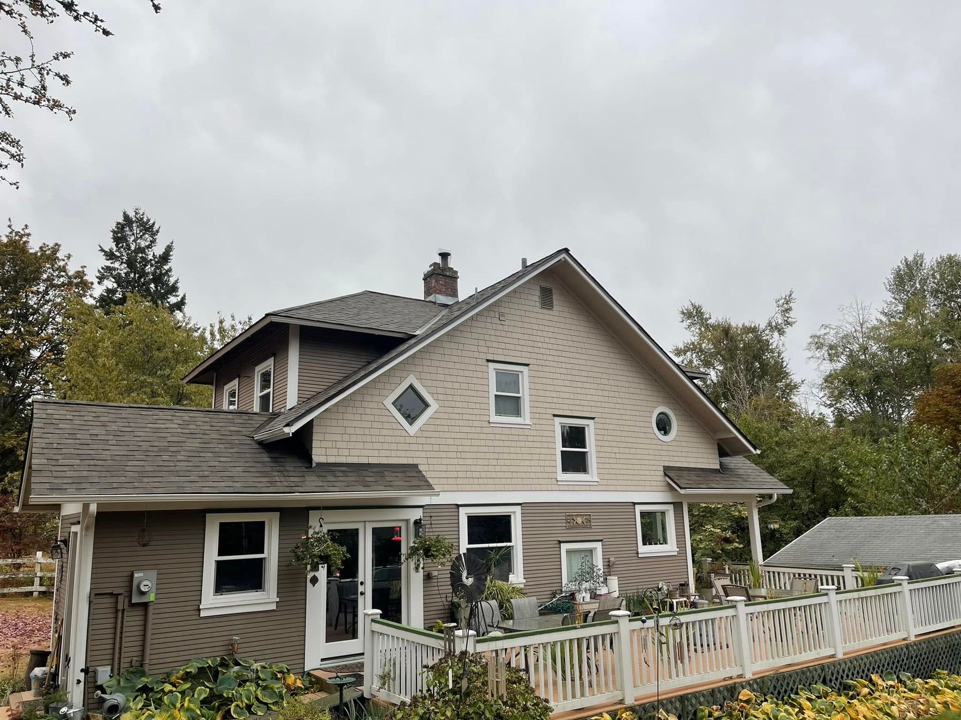 Two-story beige house with white trim, porch, and white fence under a cloudy sky.