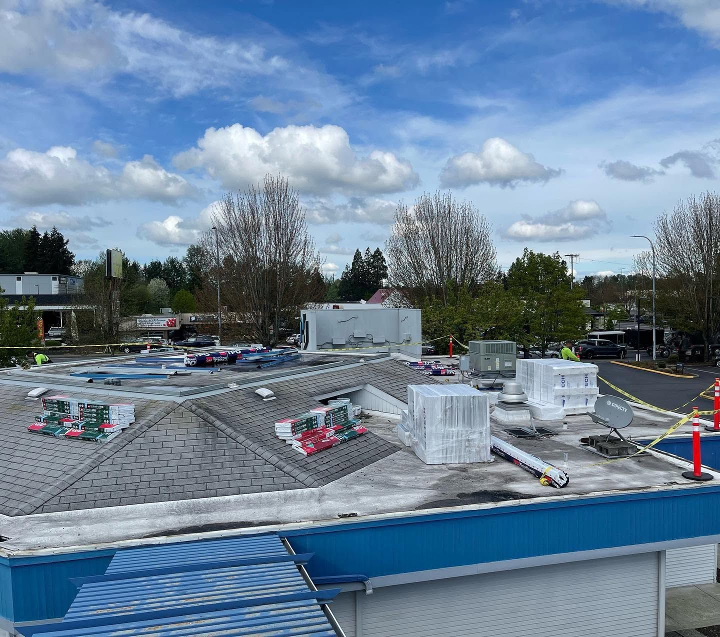 Construction site with gray roof under blue sky, wrapped materials, and scattered supplies on top