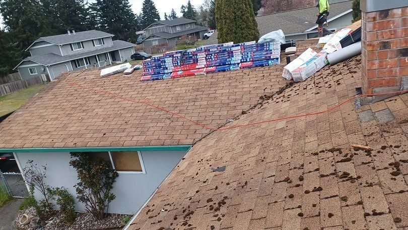 Partially repaired roof with stacked shingles and workers on top at a house site