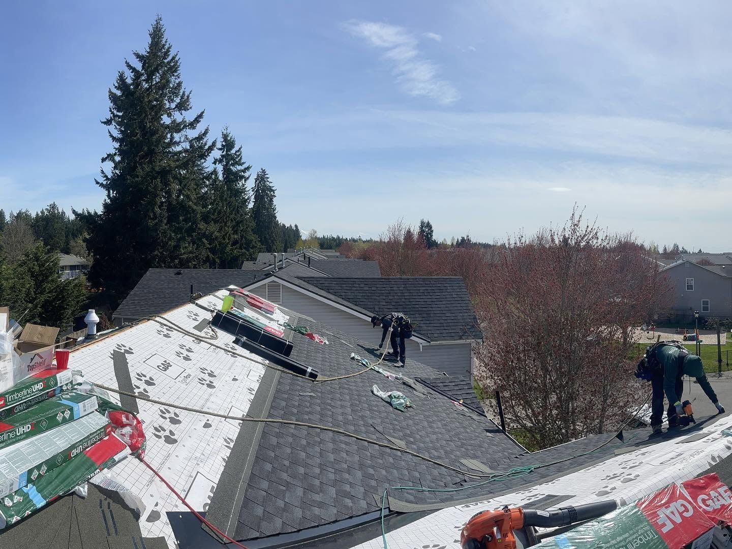 Roofers installing gray shingles on a house roof under a bright sky