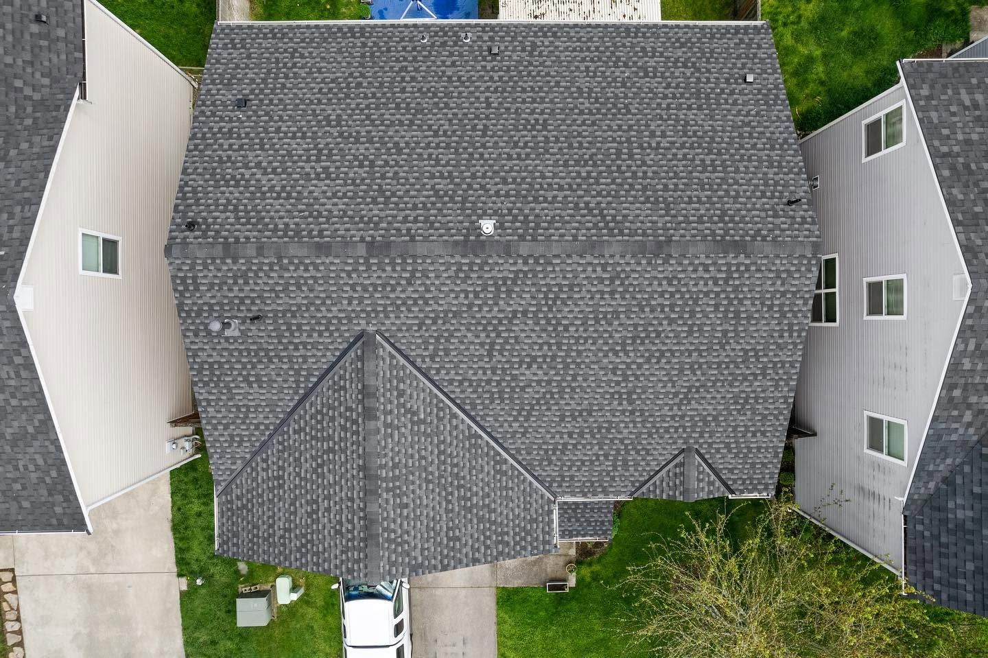 Aerial view of a house with a gray shingled roof and surrounding green lawn.