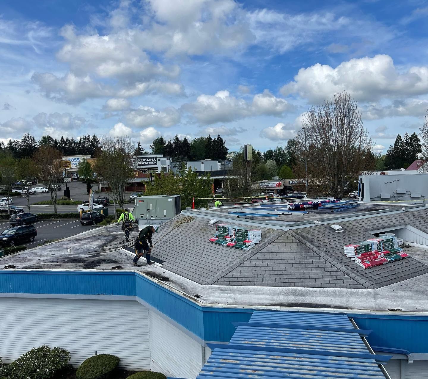 Rooftop with workers under a cloudy sky, with blue trim and nearby trees.