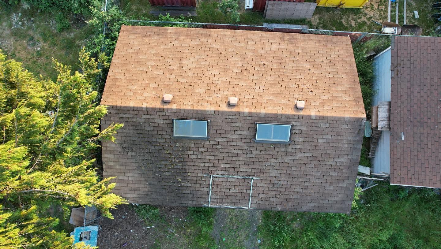 Aerial view of a tan-roofed house with two skylights beside greenery and a neighboring building.