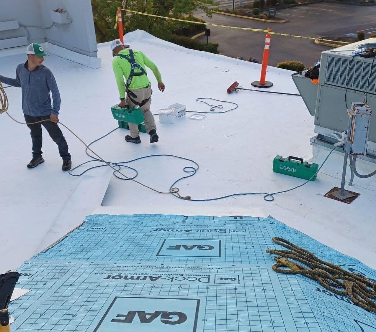 Workers installing roof insulation on a flat roof with blue panels and safety gear