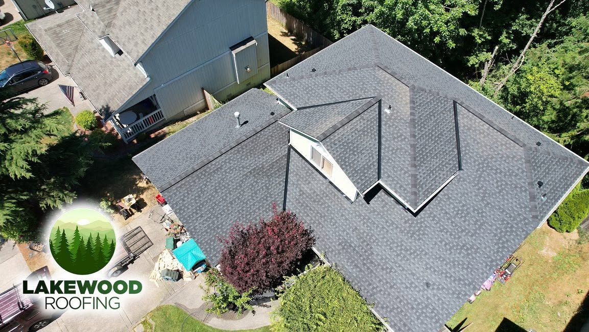 Aerial view of two homes with gray shingle roofs and trees in a suburban neighborhood