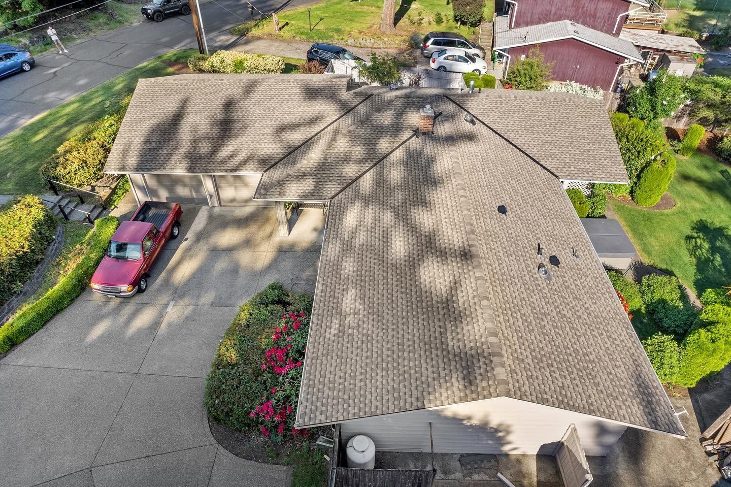 Aerial view of a tan-roofed house with a red car in the driveway and trees casting shadows across the roof.