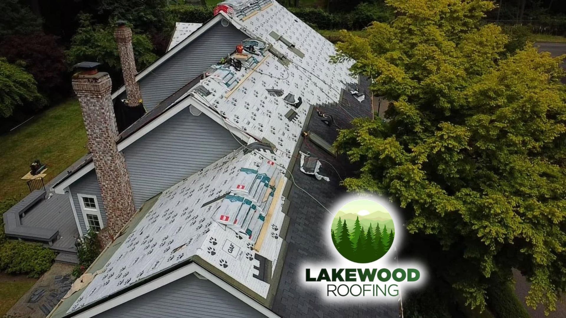 Aerial view of roofers installing shingles on a gray house, with Lakewood Roofing logo on the roof.