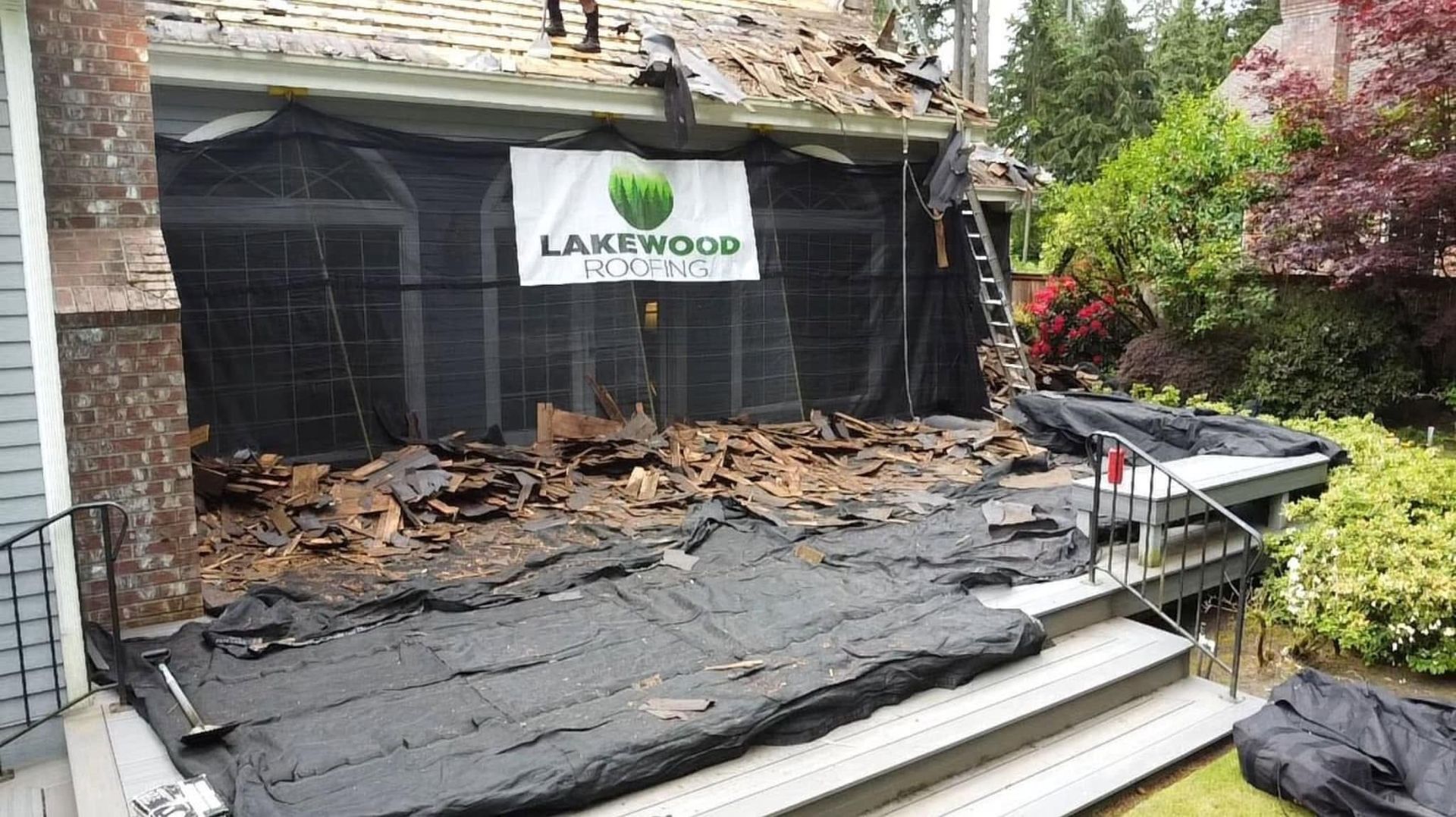 Patio covered with black tarp and fallen leaves beside a Lakwood sign on a house exterior