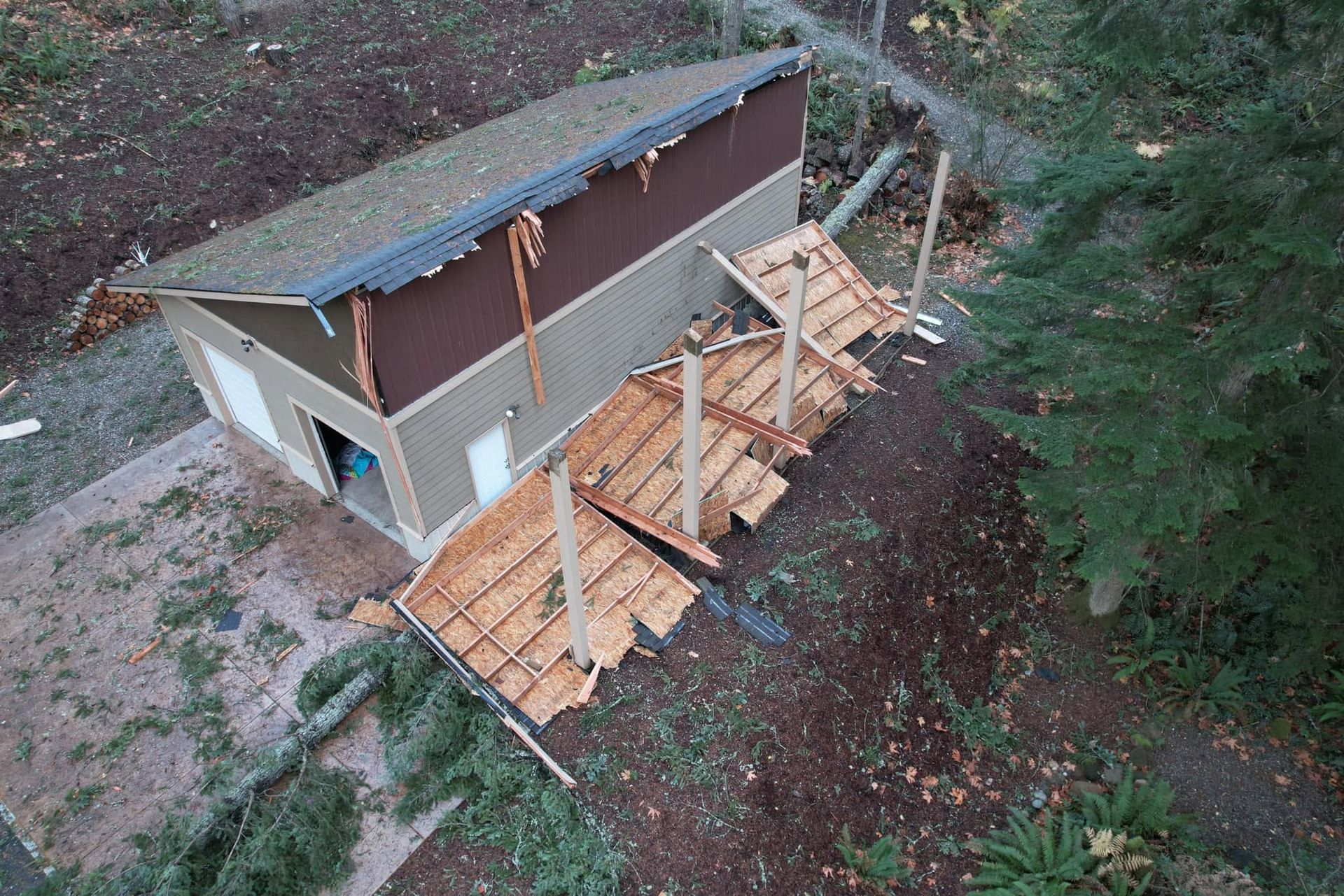 Aerial view of a small house with a damaged roof and a wooden ramp or deck under construction.