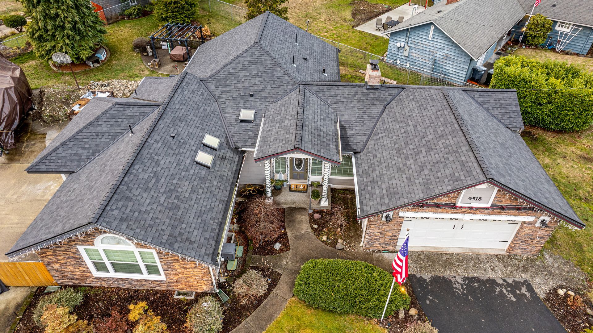 Aerial view of a suburban house with gray roof, brick exterior, driveway, and an American flag in front.