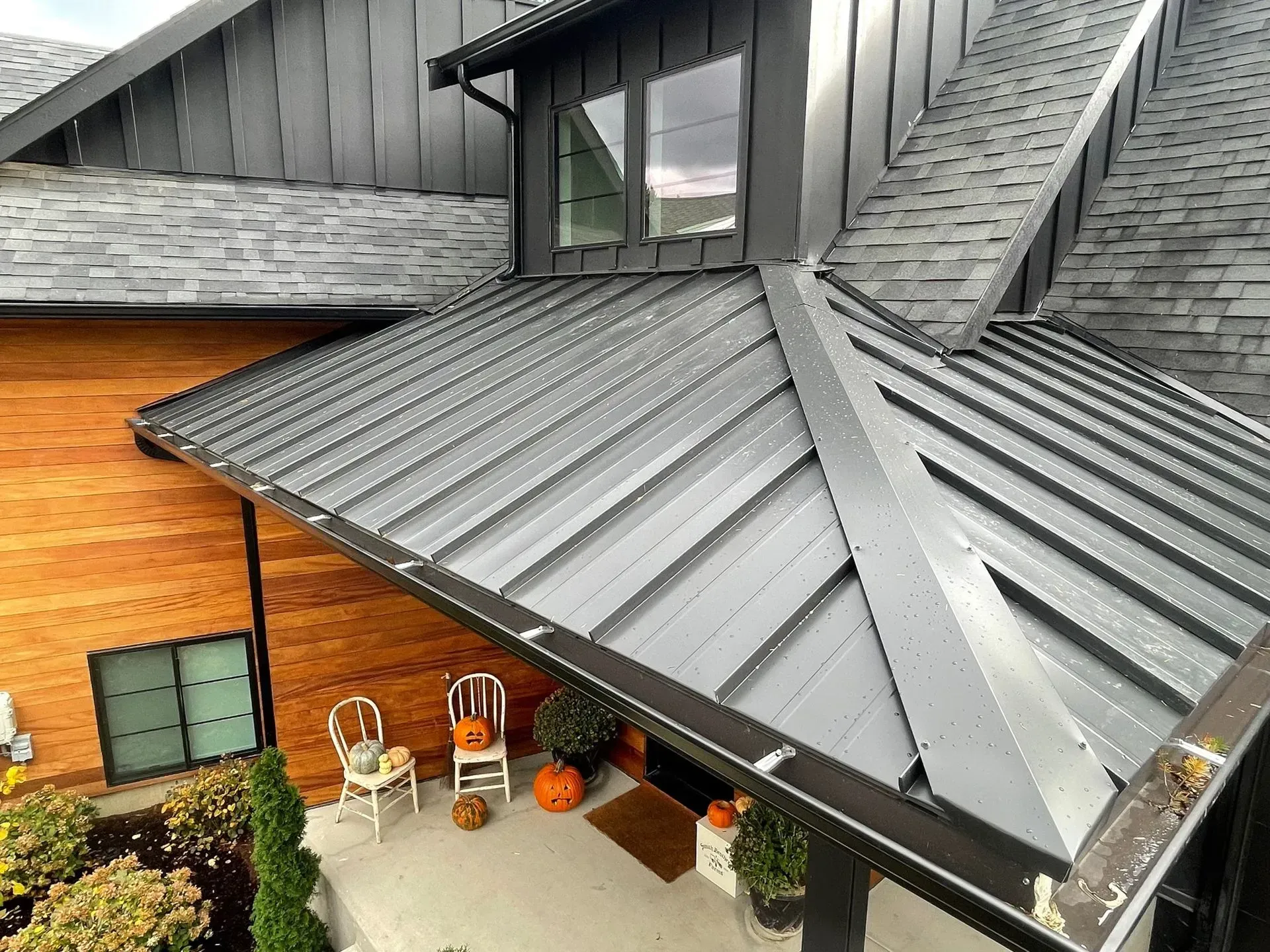 Modern house roof with dark metal panels, skylights, and a small patio below