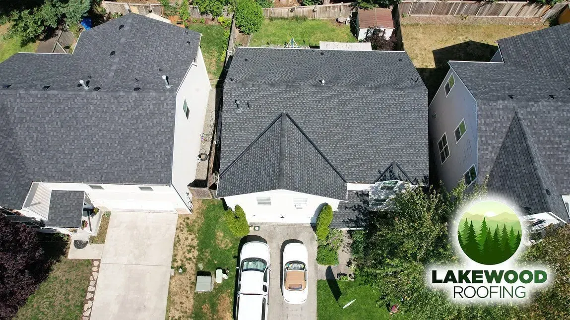 Aerial view of three suburban houses with dark roofs and driveways, one with two cars parked outside.