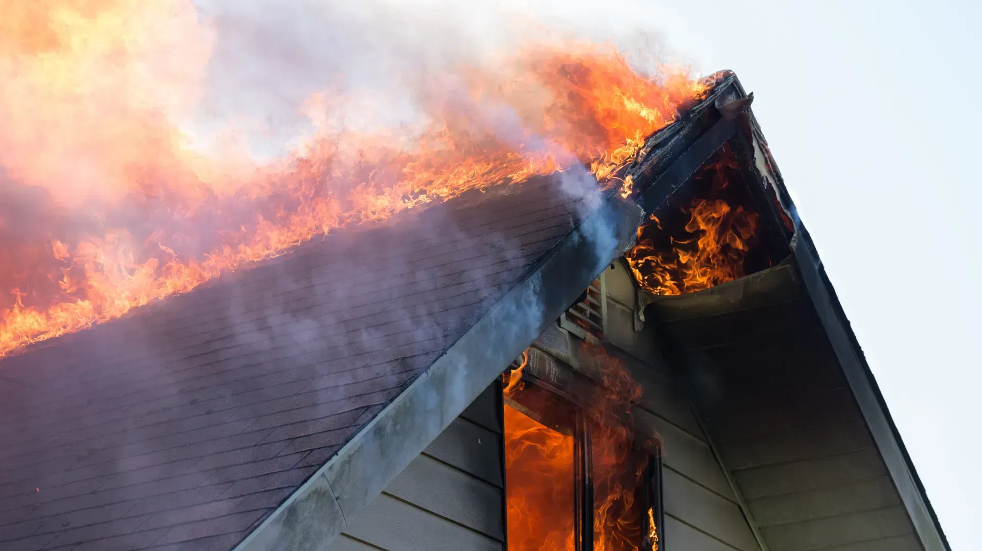 House roof engulfed in flames, with thick smoke rising from the peak