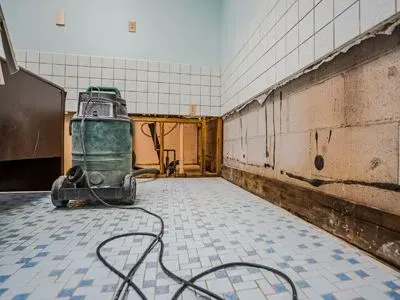 Tiled room with undergoing mold remediation with a vacuum, exposed wall framing, and coiled cord on the floor