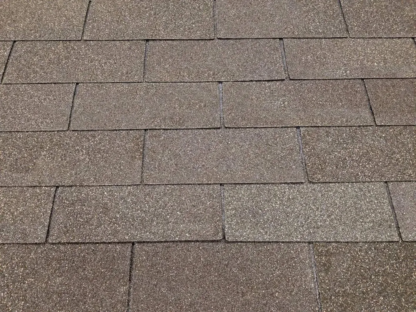 Close-up of brown asphalt roof shingles in a repeating pattern.