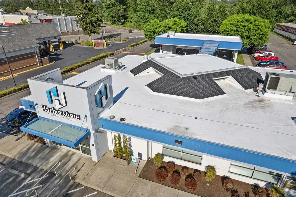 Aerial view of a white-and-blue office building with a parking lot and trees around it.