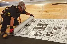 Worker installing a GAF roof underlayment sheet on a roof deck with a roller