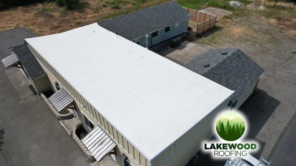 Aerial view of a large white-roofed industrial building with adjacent gray-roofed structures and parking area.