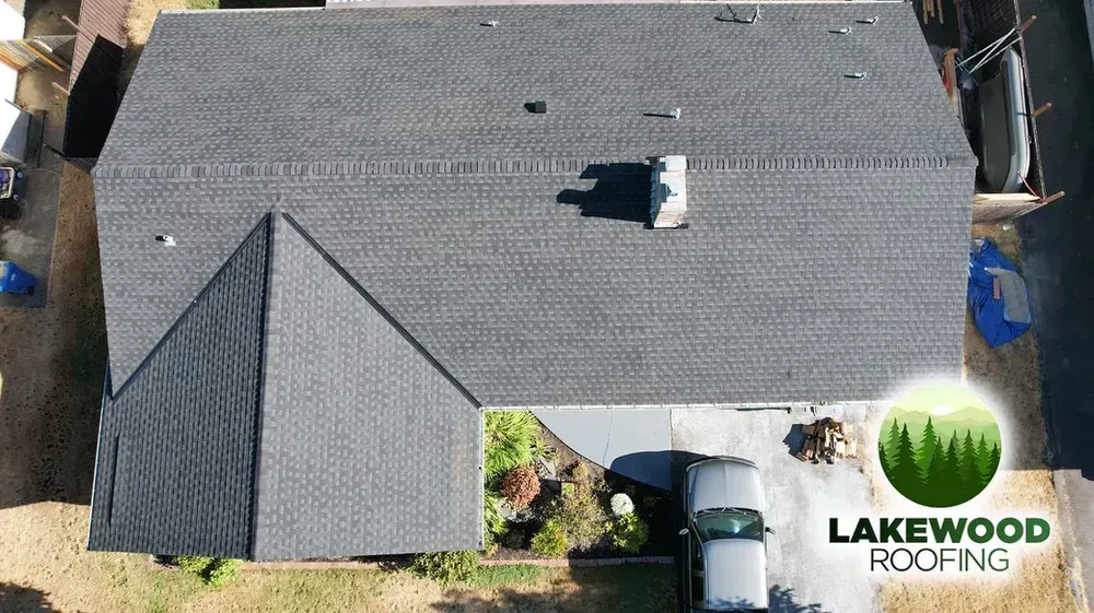 Aerial view of a gray shingle roof with storm damage and a roof repair opening, branded Lakewood Roofing.