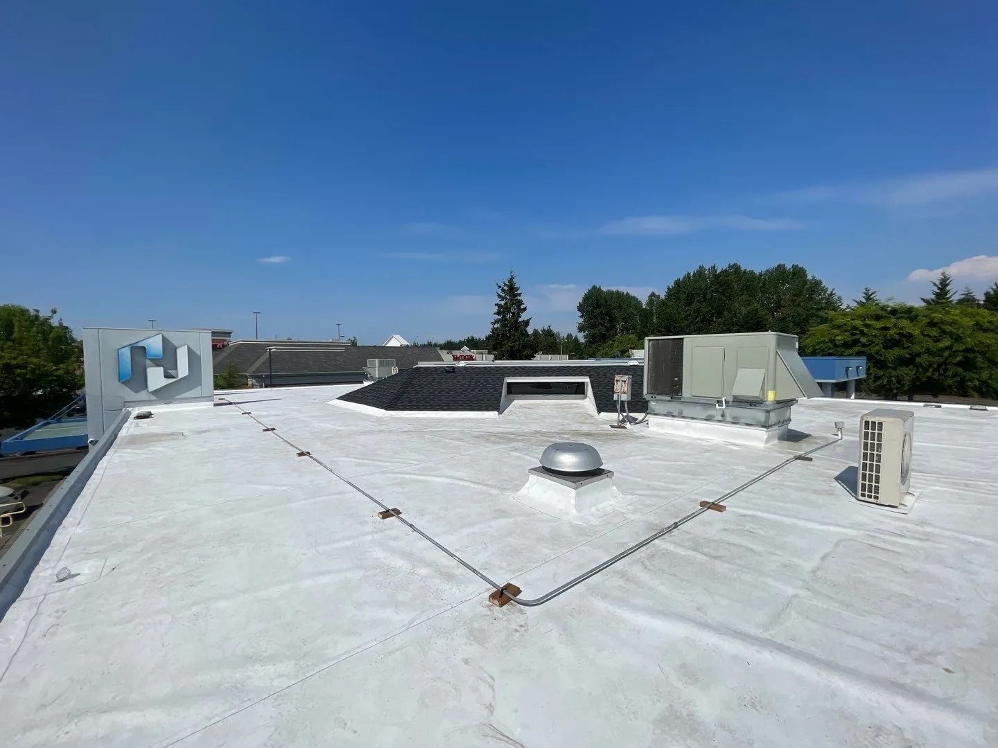 Flat white rooftop with vents and skylights under a clear blue sky