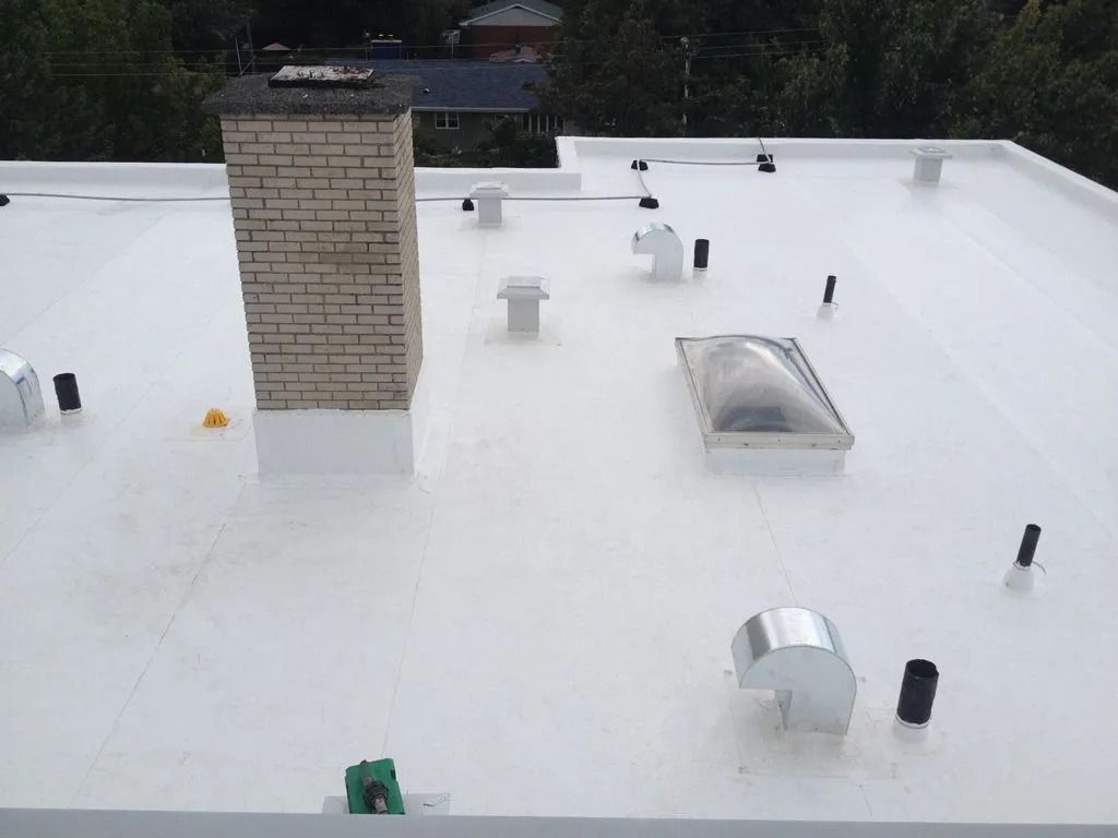 Rooftop with white coated surface, vents, chimney, and rooftop fixtures near trees in the background