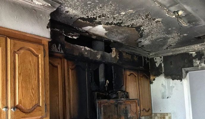 Burned kitchen cabinets and ceiling with heavy smoke damage and charring above the stove