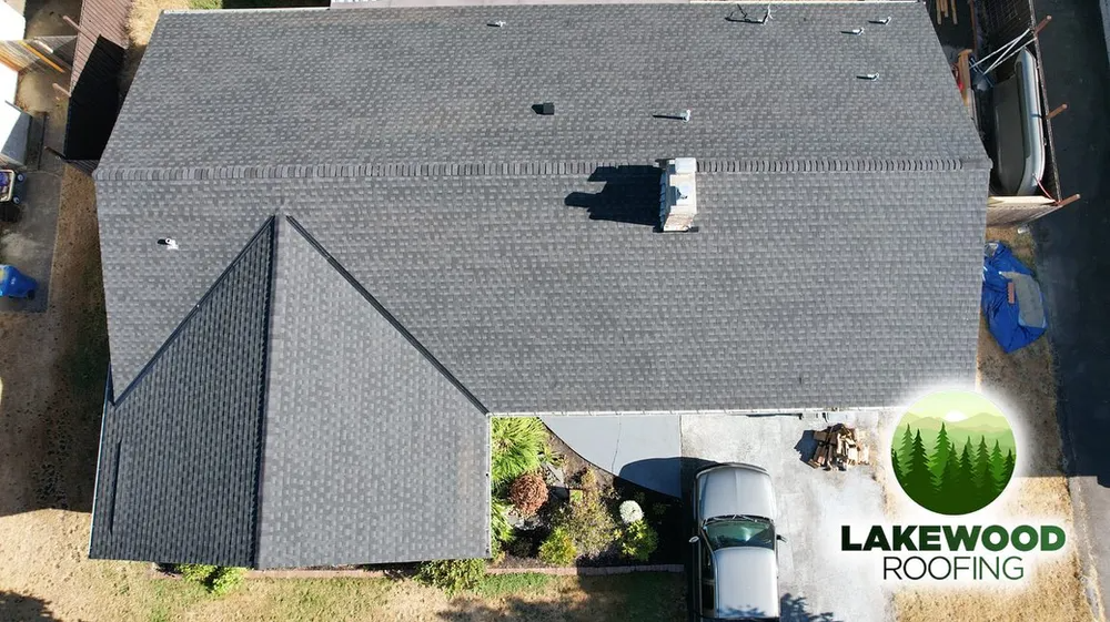 Aerial view of a dark gray shingle roof with a white vent and the Lakewood Roofing logo in the corner