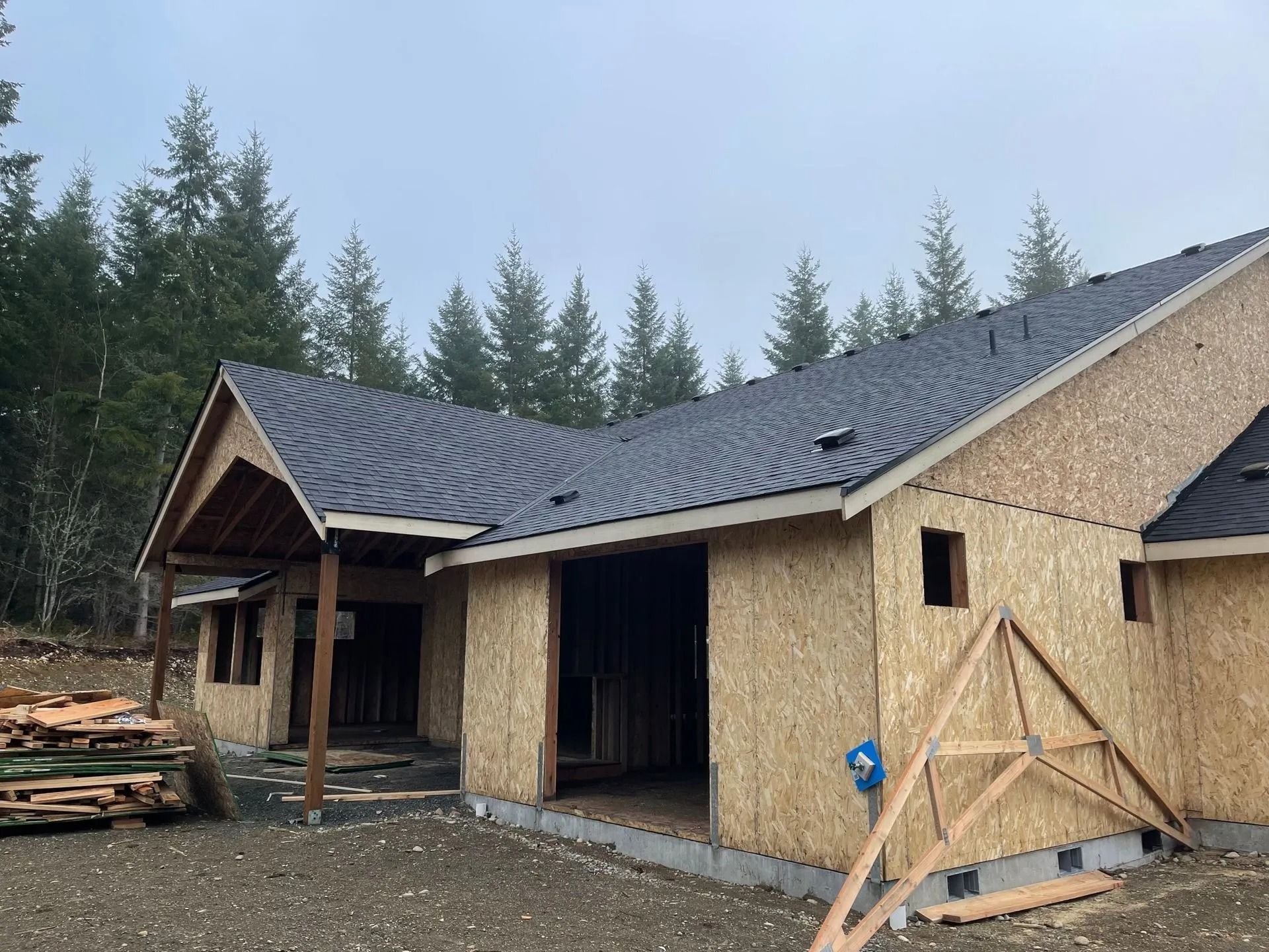 Partially built house with plywood siding and dark roof in a wooded area