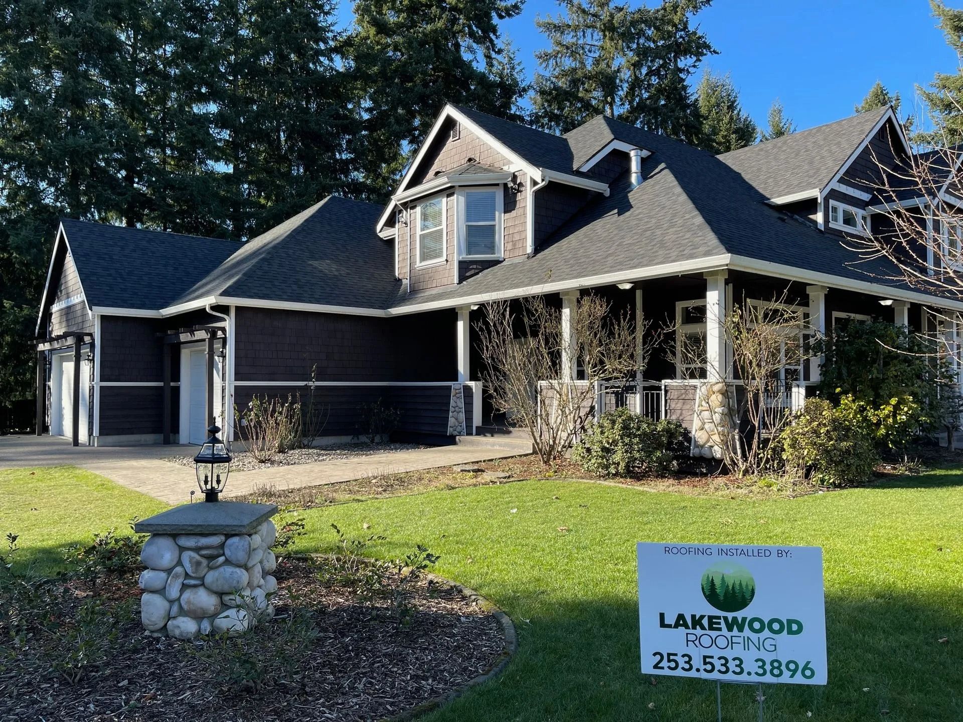 Modern dark-gray house with covered porch, stone mailbox, and Lakewood sign on a sunny lawn