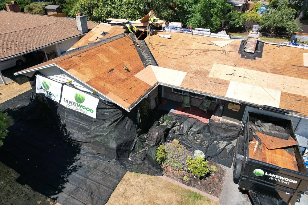 Aerial view of a dark gray shingle roof with a white vent and the Lakewood Roofing logo in the corner