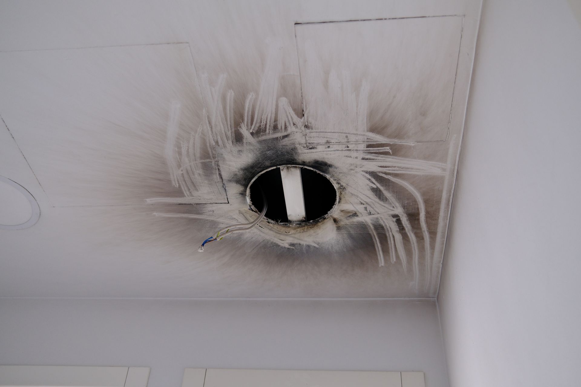 Ceiling vent with heavy soot damage and burn marks around a central hole