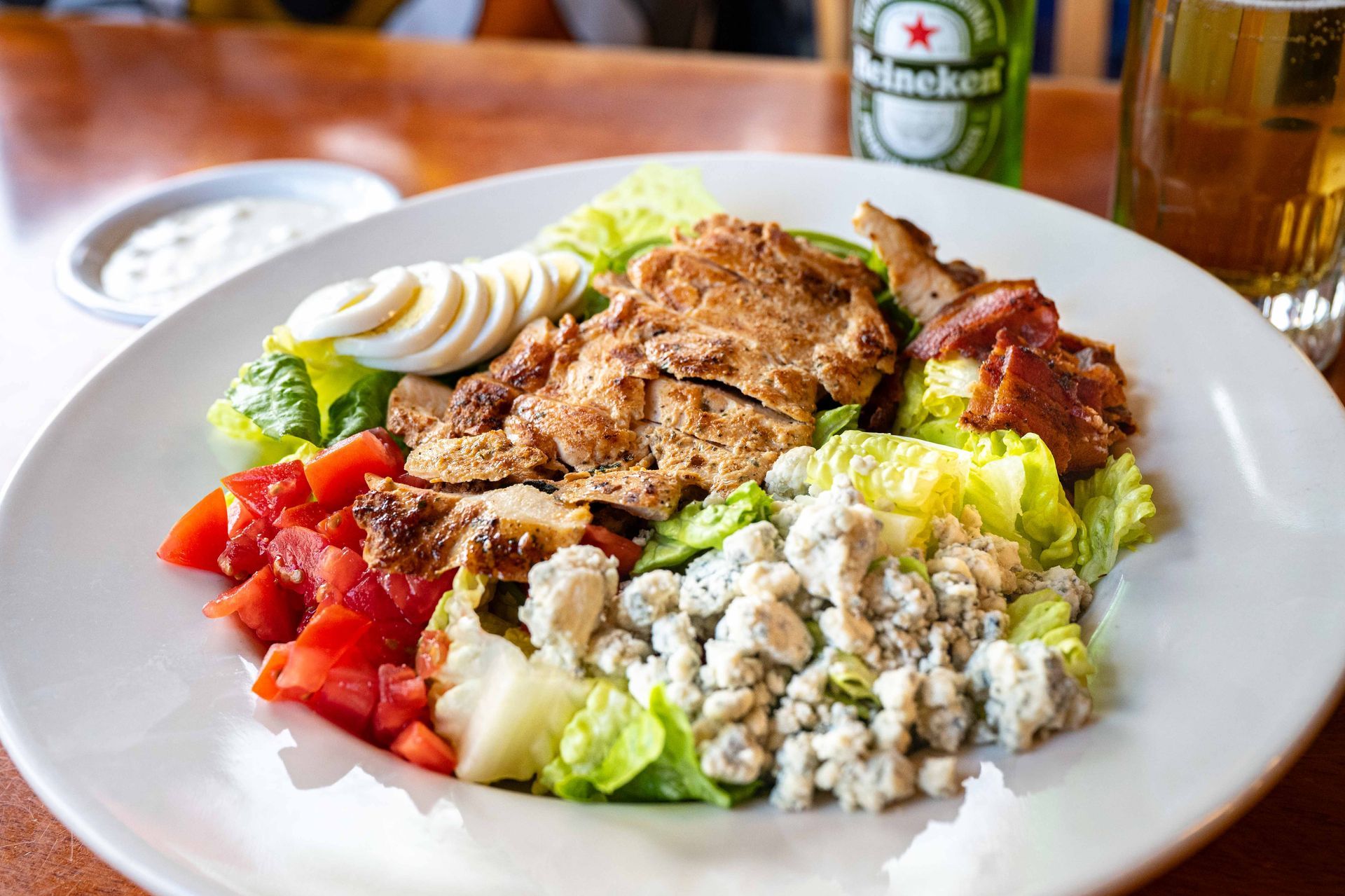 Plate of grilled meat, salad, and diced tomatoes on a white dish, with a beer glass in the background