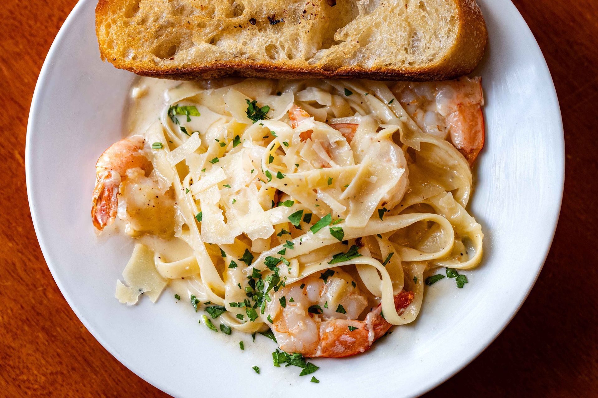 Plate of creamy fettuccine alfredo with shrimp and parsley, served with a slice of toasted bread