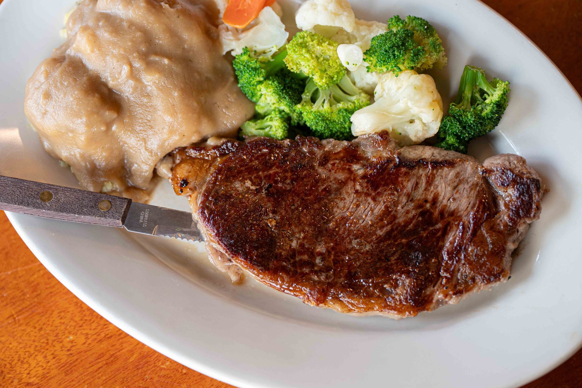 Steak with mashed potatoes and broccoli on a white plate with a fork