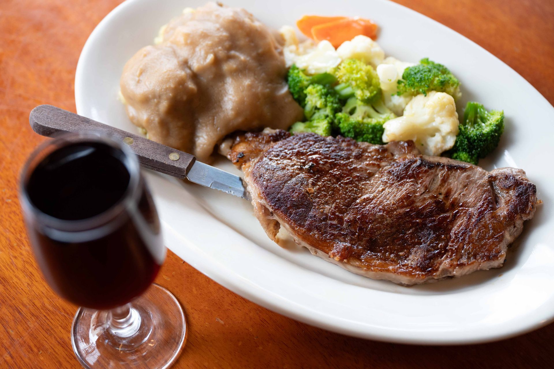 Steak dinner with mashed potatoes, broccoli, and a glass of red wine on a white plate