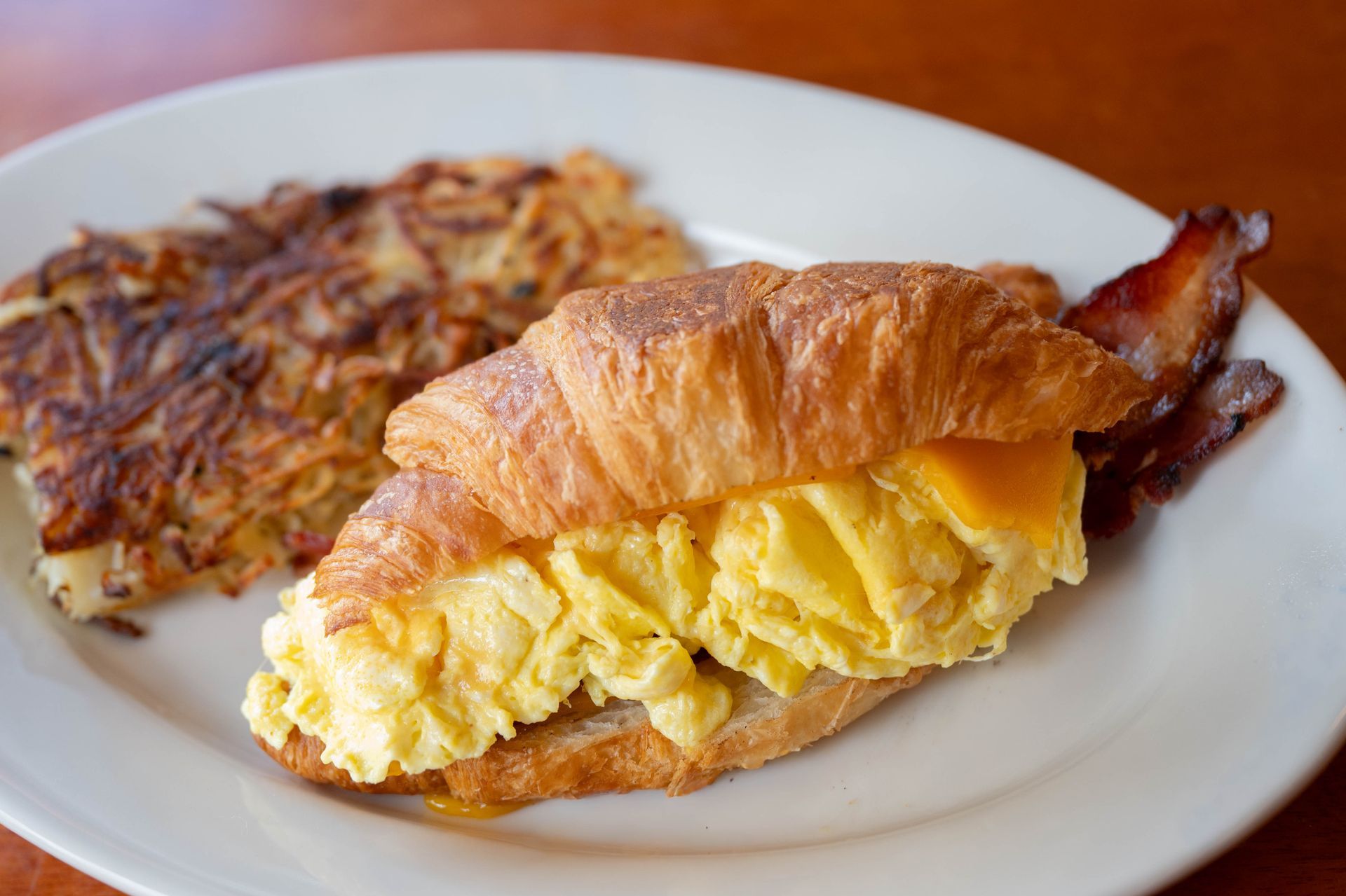 Croissant sandwich with scrambled eggs and bacon on a white plate